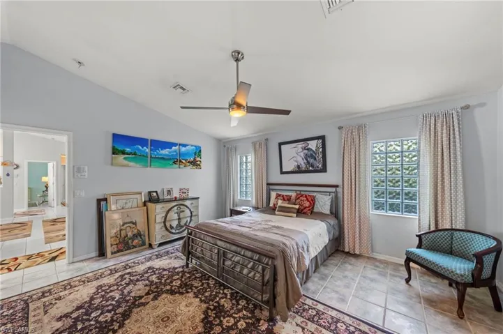 Vaulted ceiling bedroom featuring a ceiling fan with integrated lighting, ceramic tile flooring, and glass block windows providing natural light