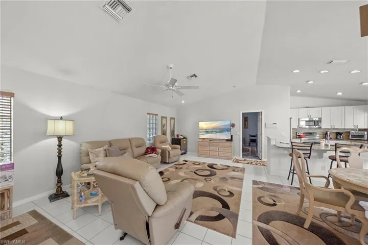 Open-concept living area featuring white tile flooring, vaulted ceilings, a ceiling fan, and recessed lighting
