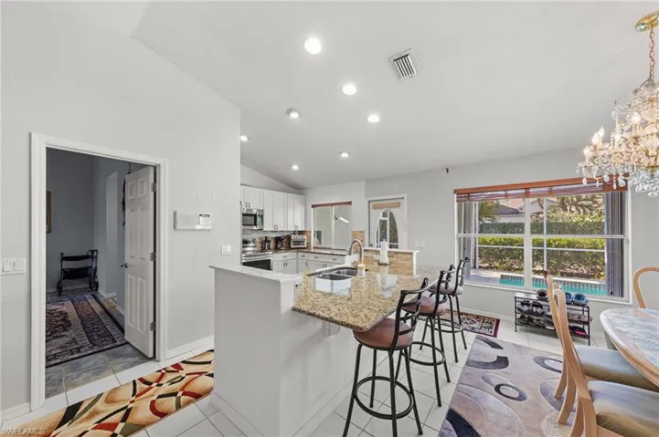 Kitchen featuring white cabinetry, granite countertops, an island with bar seating, and a large window overlooking a pool area
