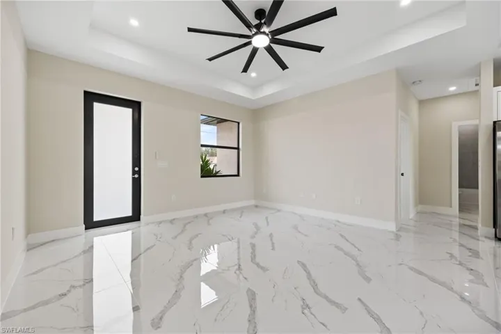 Unfurnished room with a raised ceiling, a ceiling fan, light marble finish floors, and recessed lighting