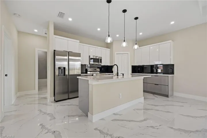 Kitchen with stainless steel appliances, light stone counters, decorative light fixtures, modern cabinets, and two tone cabinets
