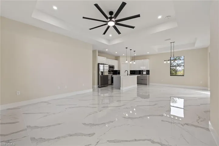 Unfurnished living room with a ceiling fan, a raised ceiling, suspended lighting, and light marble finish flooring