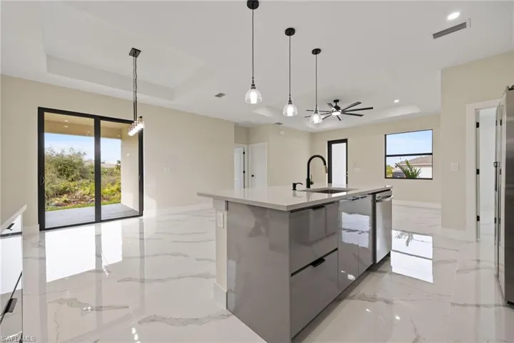 Kitchen with a tray ceiling, a center island with sink, modern cabinets, light marble finish flooring, and light stone counters