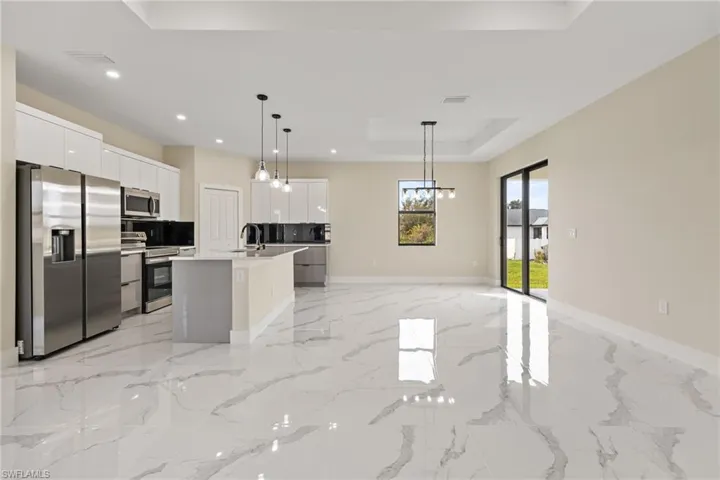 Dual tone kitchen featuring a raised ceiling, stainless steel appliances, open floor plan, a center island with sink, and light stone counters