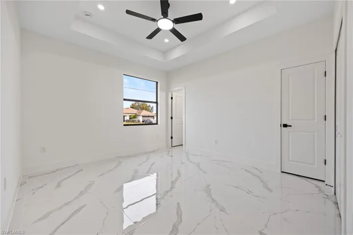 Unfurnished bedroom with a ceiling fan, recessed lighting, light marble finish floors, and a tray ceiling