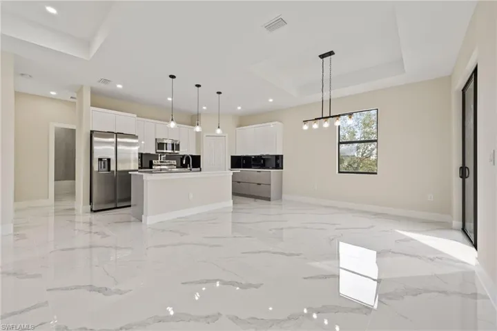 Kitchen featuring open floor plan, stainless steel appliances, white cabinets, light countertops, and an island with sink