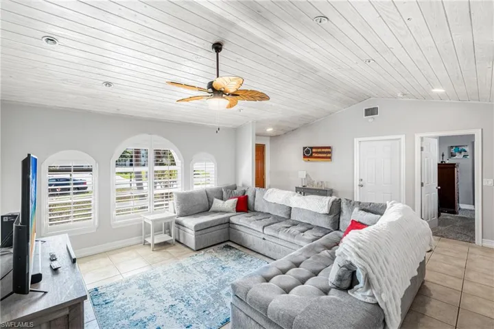 Living room with light tile patterned flooring, a ceiling fan, wood ceiling, vaulted ceiling, and baseboards