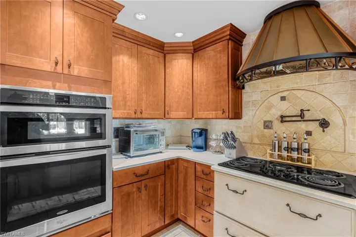 Kitchen featuring double oven, premium range hood, light countertops, black electric stovetop, and decorative backsplash