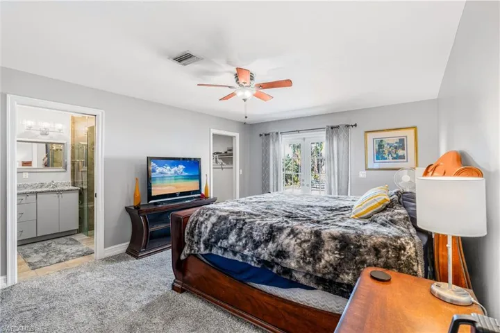 Bedroom with ensuite bath, a spacious closet, ceiling fan, baseboards, and light carpet