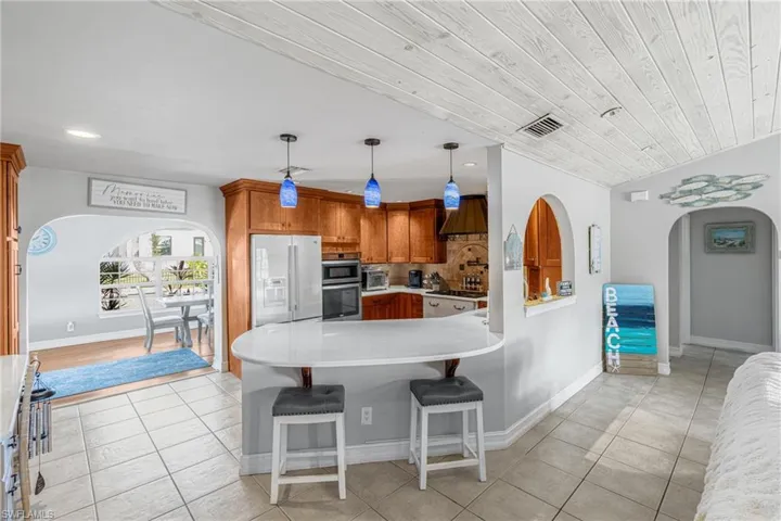 Kitchen with appliances with stainless steel finishes, custom range hood, a peninsula, arched walkways, and light tile patterned floors