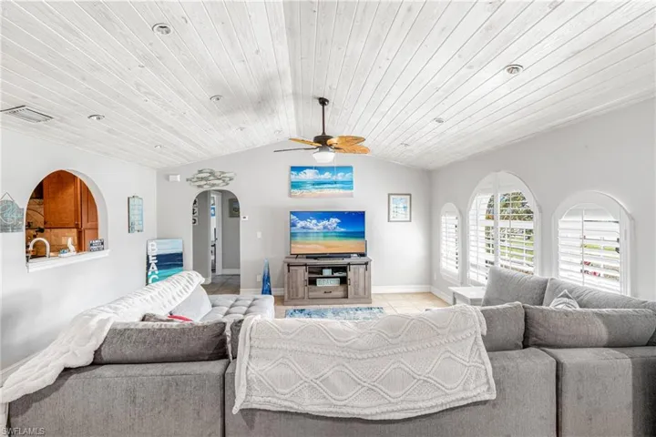 Living area with ceiling fan, arched walkways, baseboards, lofted ceiling, and wood ceiling