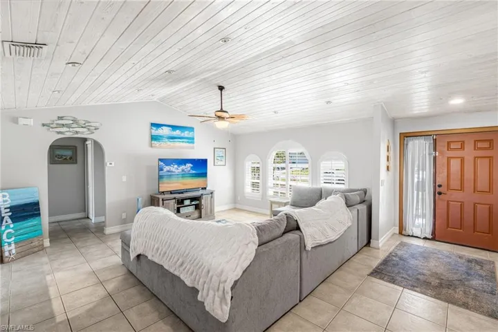 Living room with wooden ceiling, light tile patterned flooring, arched walkways, ceiling fan, and vaulted ceiling
