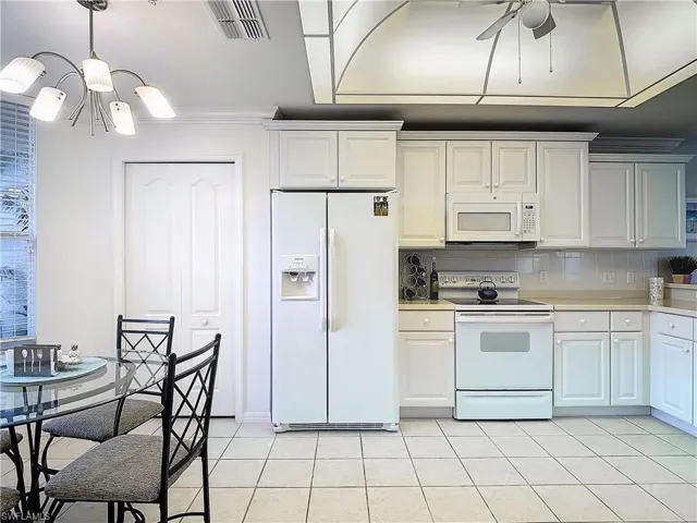 Kitchen with white cabinetry, tasteful backsplash, white appliances, and light tile patterned floors
