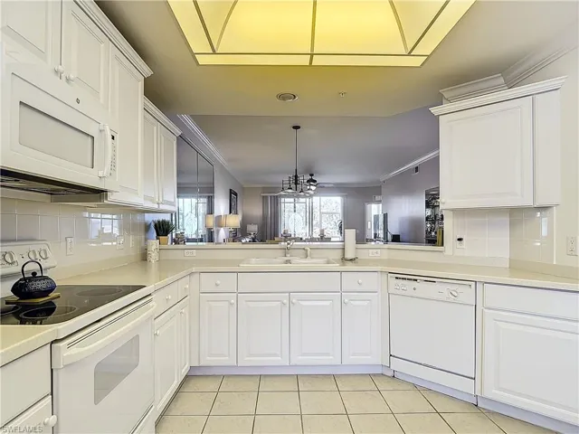 Kitchen with backsplash, kitchen peninsula, white appliances, and ornamental molding