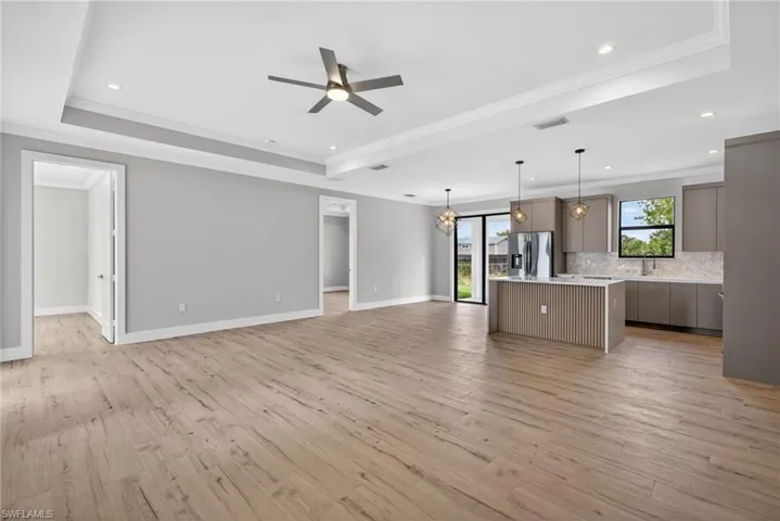 Spacious open-concept interior featuring wood-look flooring, tray ceilings with recessed lighting, and a contemporary ceiling fan