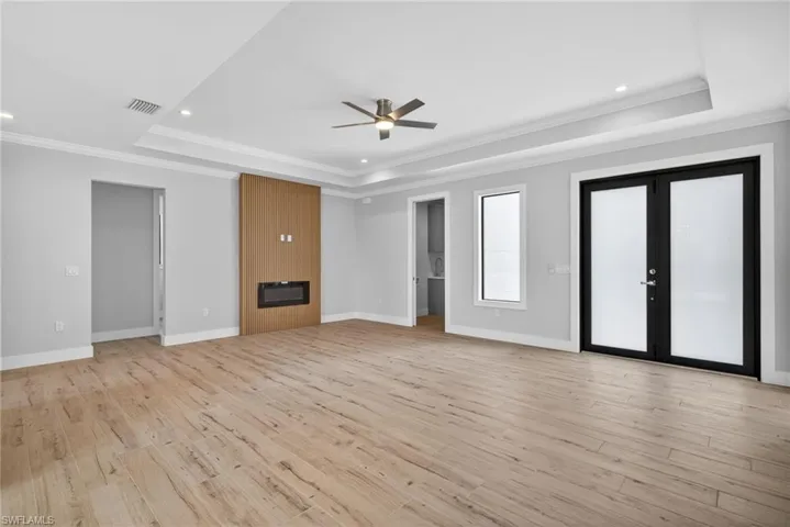 Spacious room featuring wood-finish flooring, a contemporary built-in fireplace with wood paneling, a tray ceiling with recessed lighting, and a ceiling fan