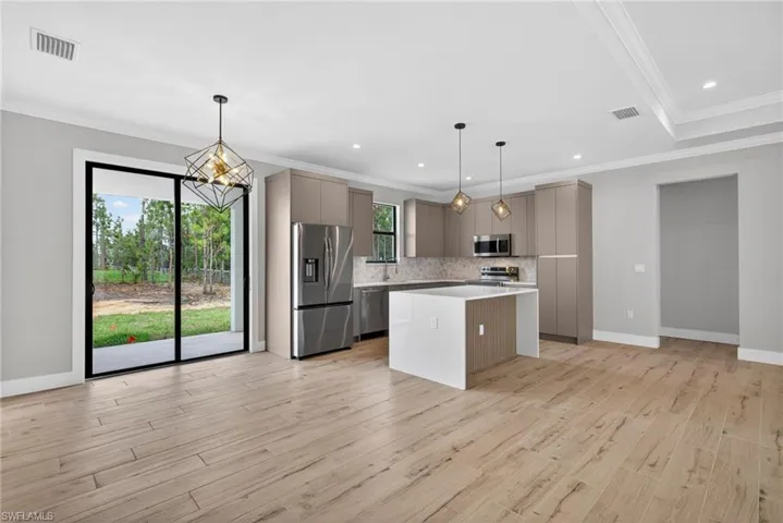 Open-concept kitchen and living area featuring wood-finish flooring, a kitchen island with a waterfall countertop, stainless steel appliances, and contemporary pendant lighting