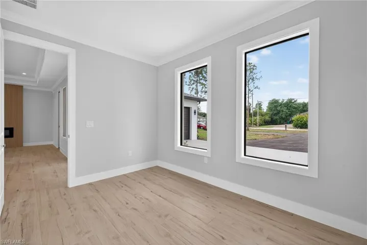 Light-filled interior featuring two large windows, light wood-finish flooring, crisp white trim, and a tray ceiling visible in the adjacent space