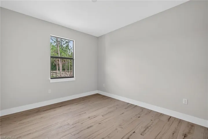 Interior room featuring a window with black trim, wood-finish flooring, light grey painted walls, and white baseboards