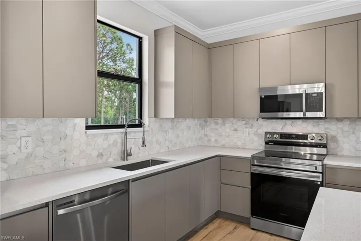Modern kitchen featuring flat-panel cabinetry, white solid surface countertops, and a hexagonal tile backsplash