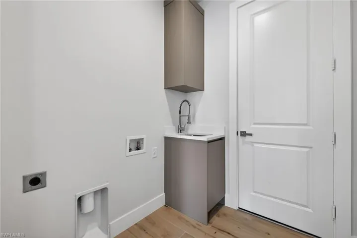 Utility area featuring a built-in sink with a gooseneck faucet, light-colored cabinetry, and wood-finish flooring