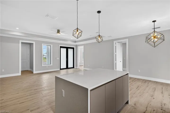 Contemporary kitchen island with a light-toned countertop, wood-finish flooring, modern pendant lighting, French doors, and a ceiling fan