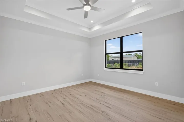 Spacious interior room featuring light wood-finish flooring, a tray ceiling with recessed lighting, and a contemporary ceiling fan