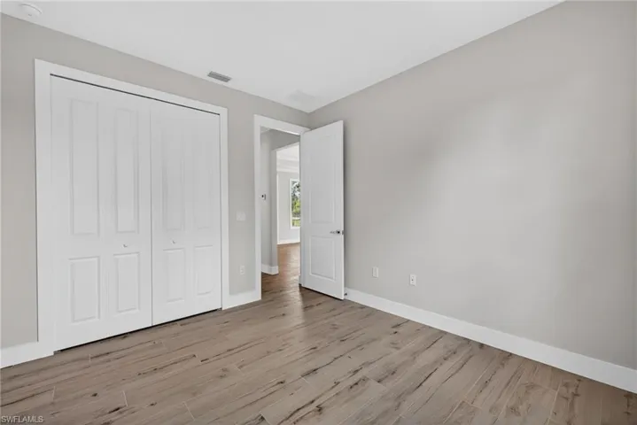 Room featuring wood-finish flooring, light gray wall paint, white baseboards, and a bi-fold closet