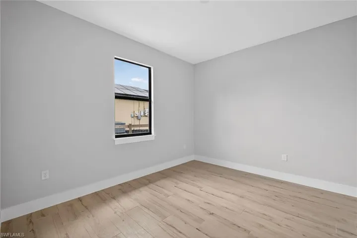 Neutral-toned room with light wood-finish flooring, crisp white baseboards, and a single black-framed window