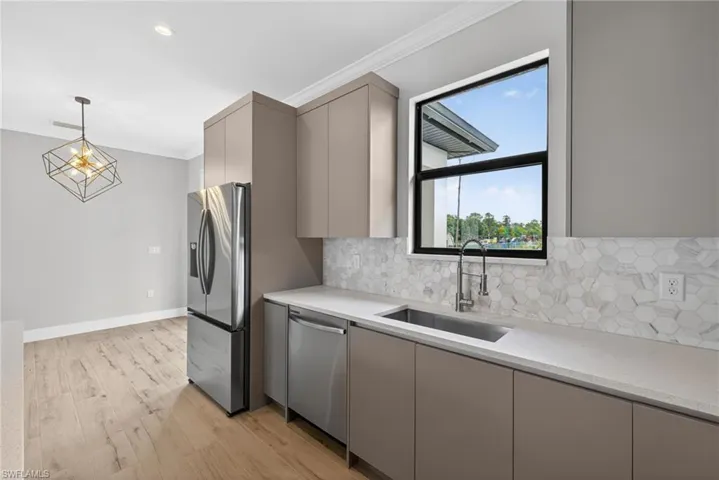 Modern kitchen with sleek flat-panel cabinetry, stainless steel appliances, white quartz countertops, and a full-height hexagonal tile backsplash