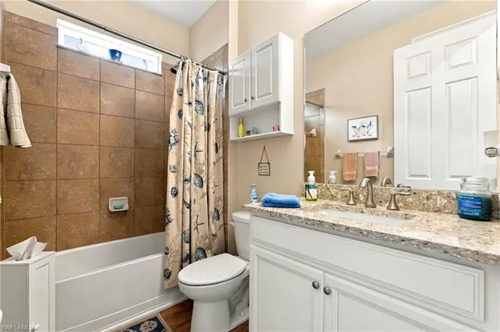 Bathroom featuring a vanity with a stone-finish countertop, white cabinetry with matching built-in wall storage, a shower-tub combination with oversized tile surround, and an integrated wall mirror