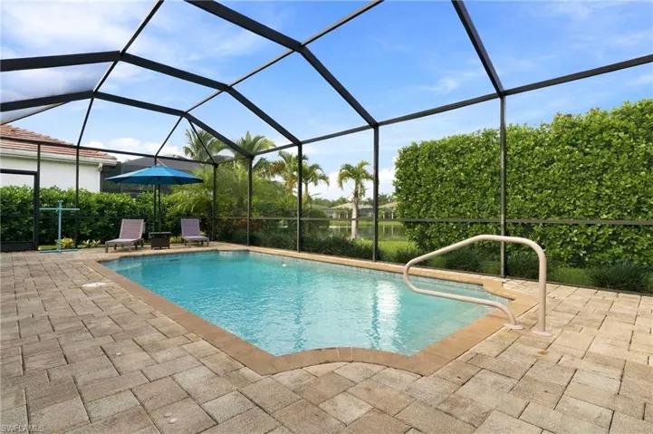 Screen-enclosed swimming pool with stone-paver decking, metal pool railing, and hedge-lined perimeter