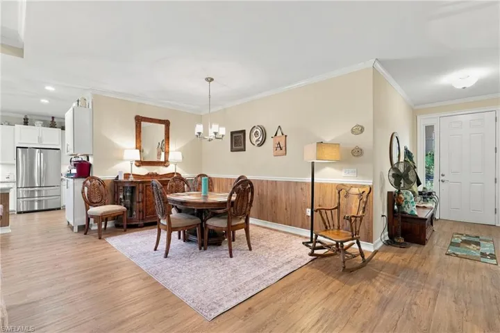 Dining area featuring wood-finish wainscoting, wood-finish flooring, a multi-light chandelier, and crown molding