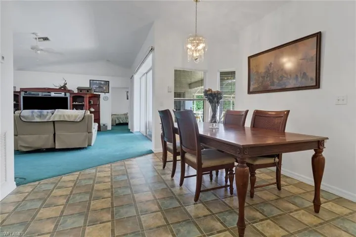 Carpeted dining room featuring ceiling fan with notable chandelier and lofted ceiling