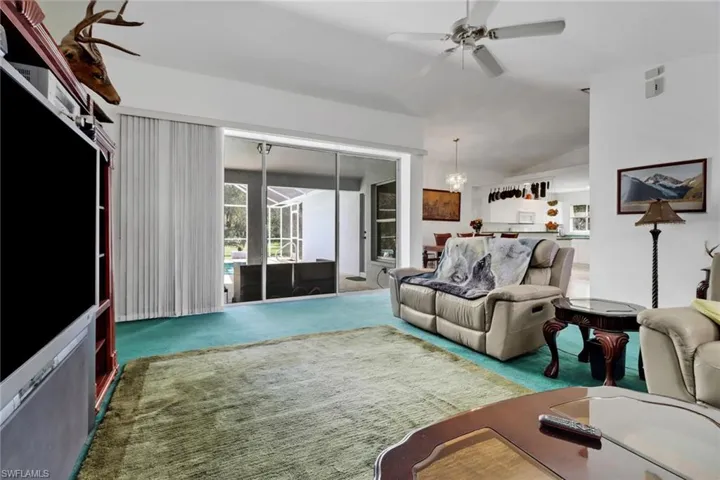 Carpeted living room with ceiling fan with notable chandelier and vaulted ceiling