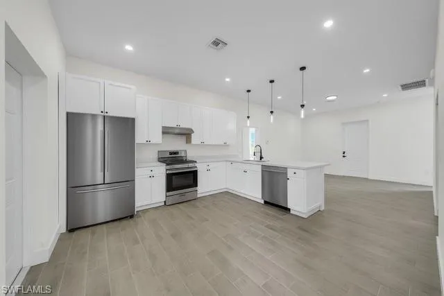 Kitchen featuring stainless steel appliances, white cabinetry, light countertops, hanging light fixtures, and wood finish floors