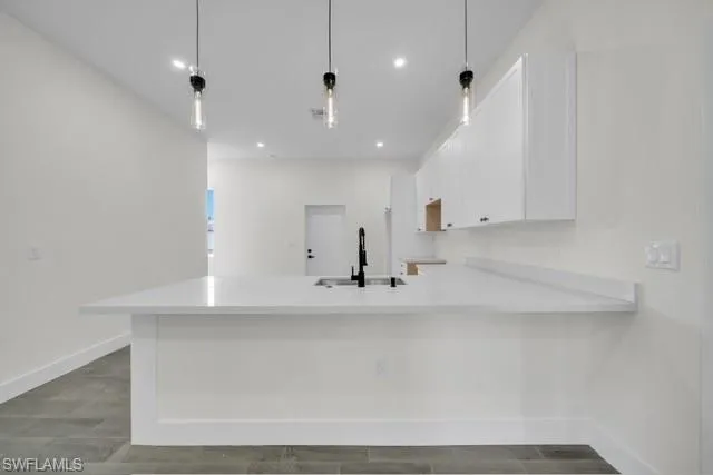 Kitchen featuring white cabinetry, a peninsula, light stone counters, pendant lighting, and wood finish floors