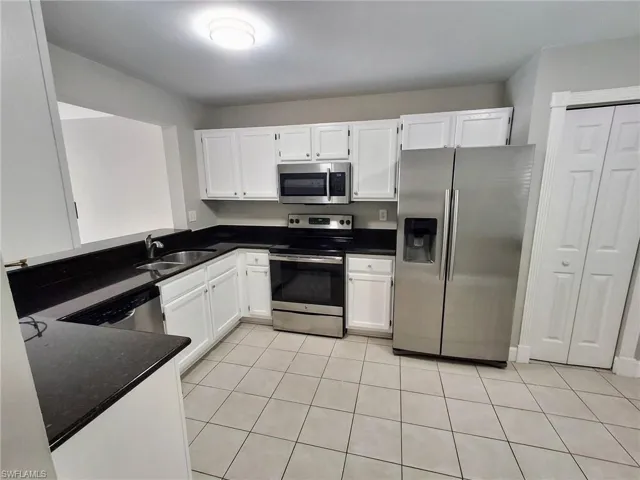 Kitchen with stainless steel appliances, white cabinetry, light tile patterned floors, and dark stone countertops