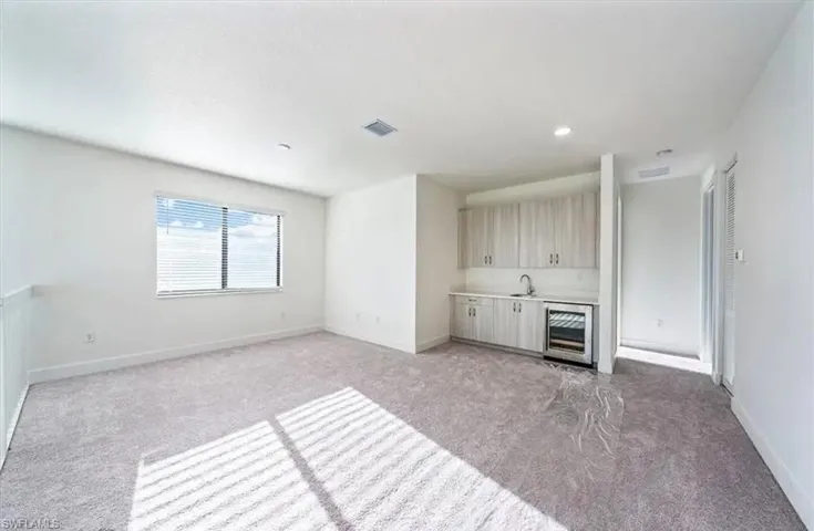 Unfurnished living room featuring light colored carpet, beverage cooler, wet bar, and recessed lighting