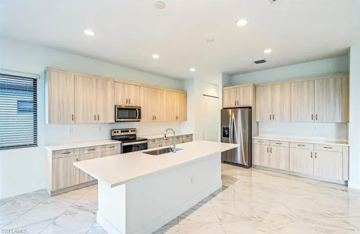 Kitchen featuring light brown cabinets, stainless steel appliances, light marble finish flooring, a kitchen island with sink, and recessed lighting