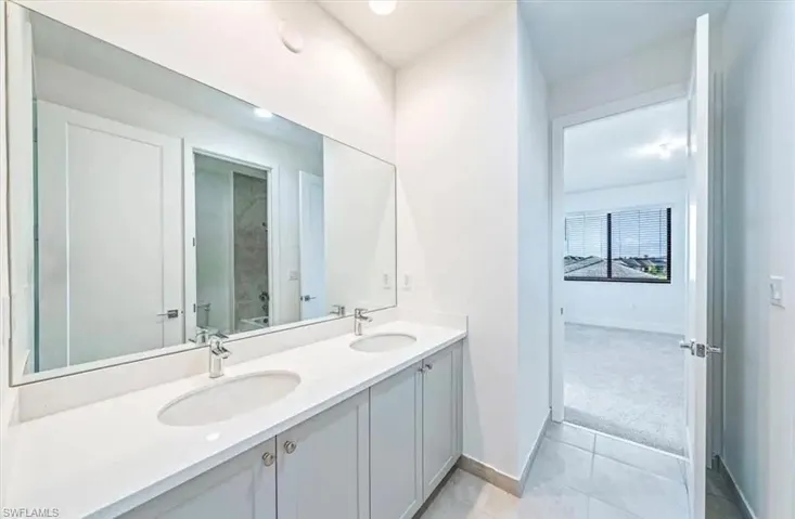 Bathroom with double vanity, light tile patterned floors, and light colored carpet