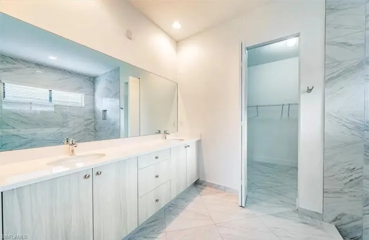 Bathroom with light marble finish flooring, double vanity, a marble finish shower, and a walk in closet