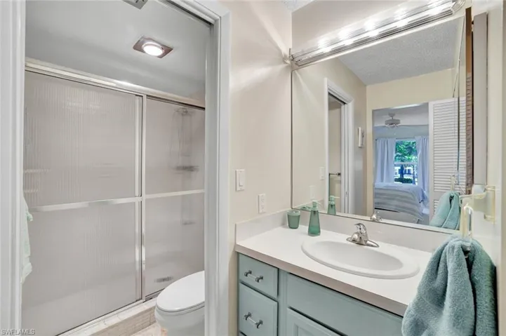 Ensuite bathroom featuring vanity, a shower stall, a textured ceiling, and ceiling fan