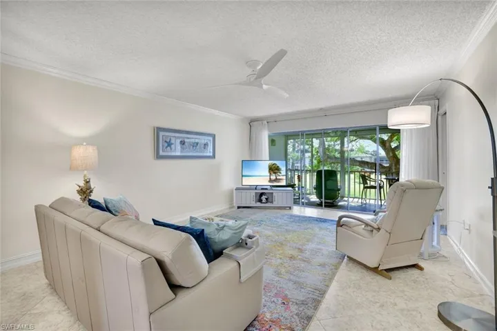 Living area with a textured ceiling, ornamental molding, a ceiling fan, and light tile patterned floors