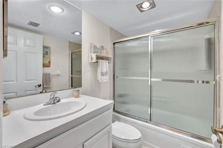 Bathroom featuring vanity, bath / shower combo with glass door, and recessed lighting