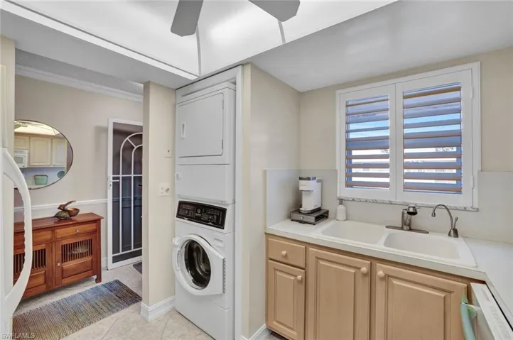 Washroom featuring stacked washing machine and dryer, light tile patterned floors, and ceiling fan