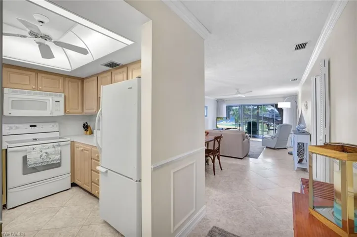 Kitchen with a ceiling fan, white appliances, light brown cabinets, light tile patterned floors, and crown molding