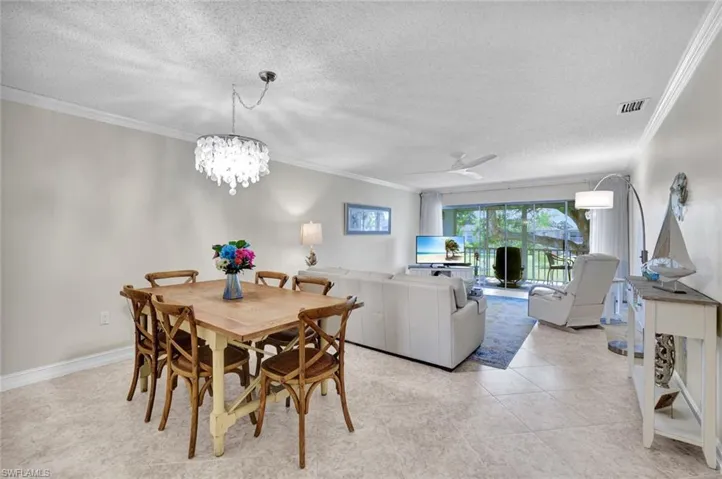 Dining room with a textured ceiling, ceiling fan, crown molding, a chandelier, and light tile patterned floors