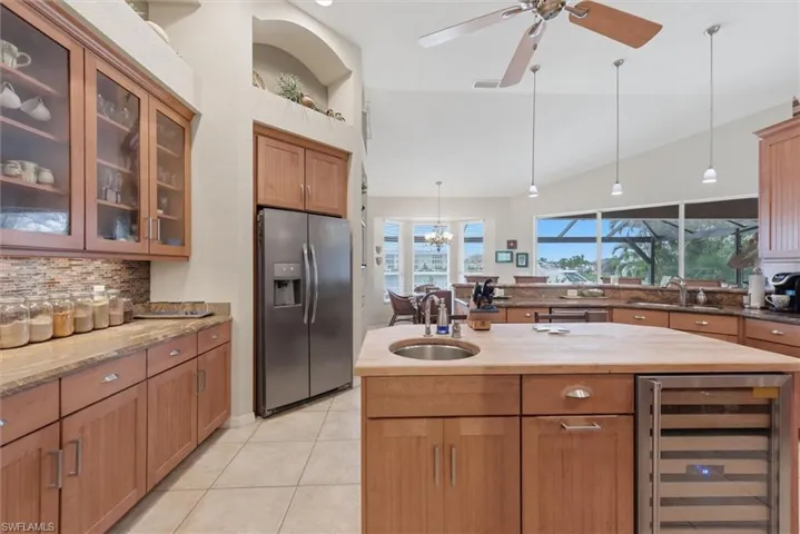 Kitchen featuring stainless steel fridge with ice dispenser, beverage cooler, glass fronted cabinets, dark stone counters, and a center island with sink