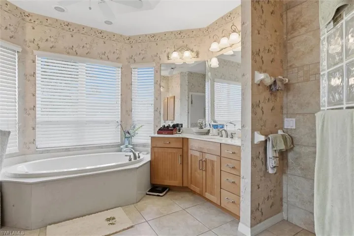 Full bathroom with vanity, light tile patterned floors, a garden tub, wallpapered walls, and ceiling fan